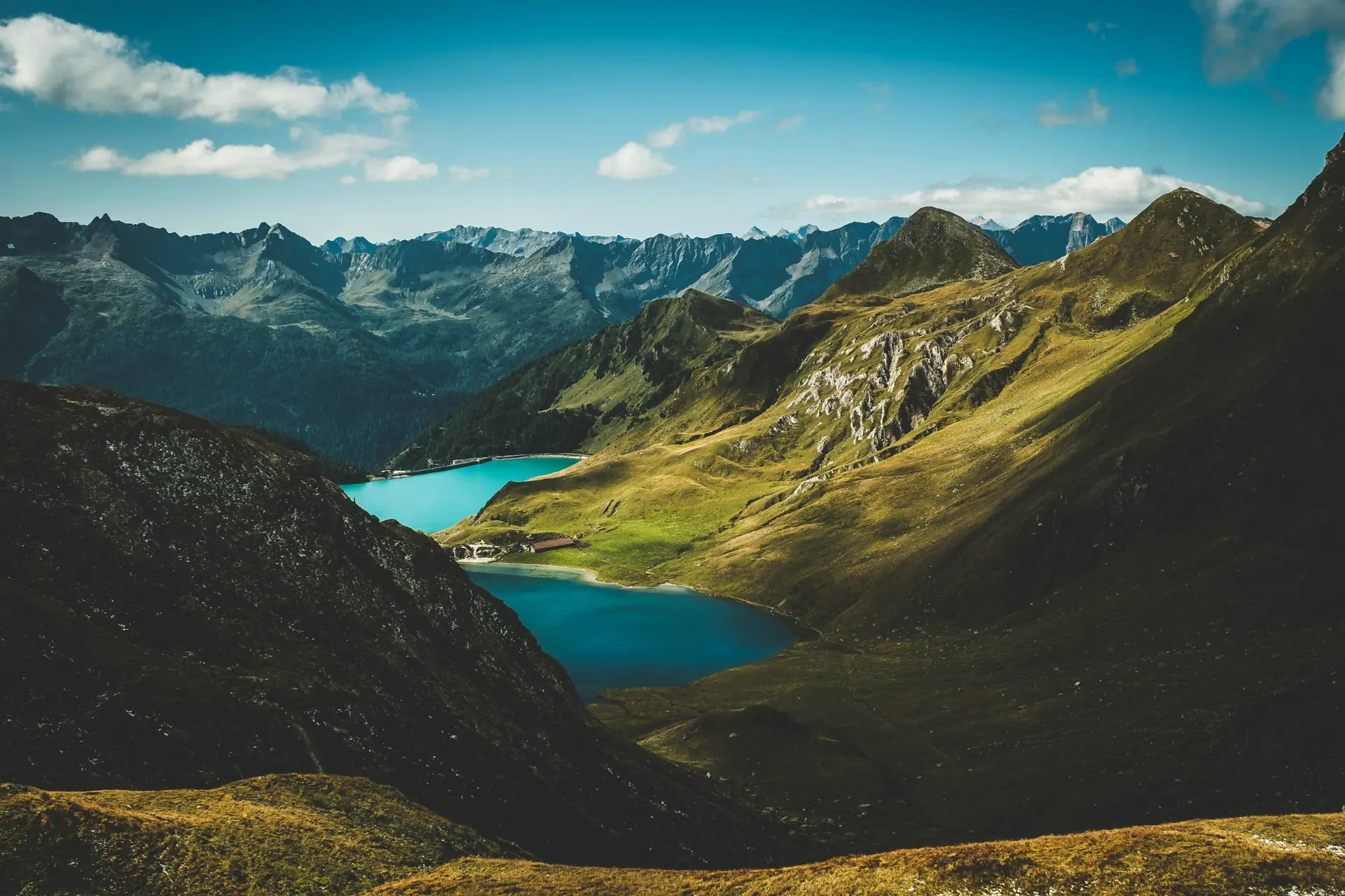 Alpine valley with turquoise lakes and green slopes under a blue sky.